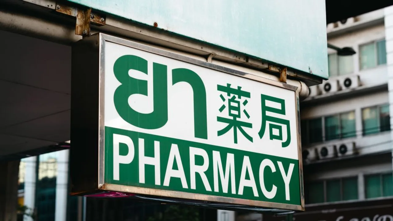 街邊藥局的懸掛式招牌，綠白配色，由上而下並排泰文「ยา」、中文「藥局」與英文 PHARMACY，背景是城市街區的建築外牆